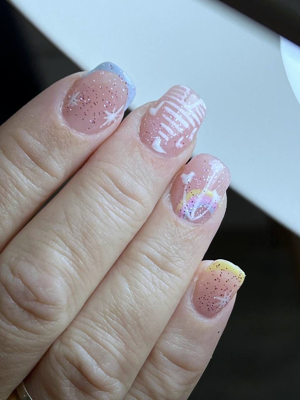 Uña corta natural con francesas en azul y amarillo pastel, glitter y dibujo a mano alzada.